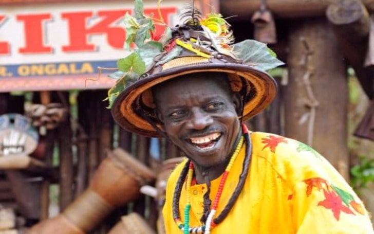 Mor Dogo Thiam smiling in a traditional hat with leaves and yellow colored Senegalese cultural dress.